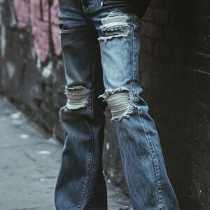 Close-up of ripped blue denim jeans with flared legs, worn in an urban alleyway.