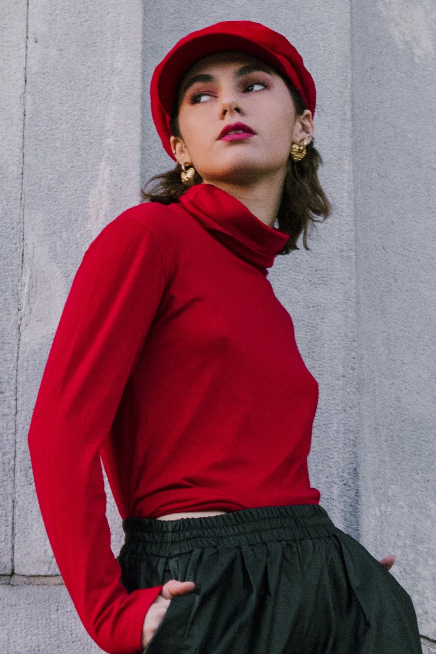 Model wearing a red long sleeves top, black pants, a red hat and red lipstick