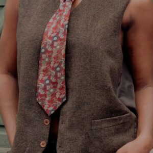 Brown textured vest worn open over a sleeveless shirt and under a floral tie.