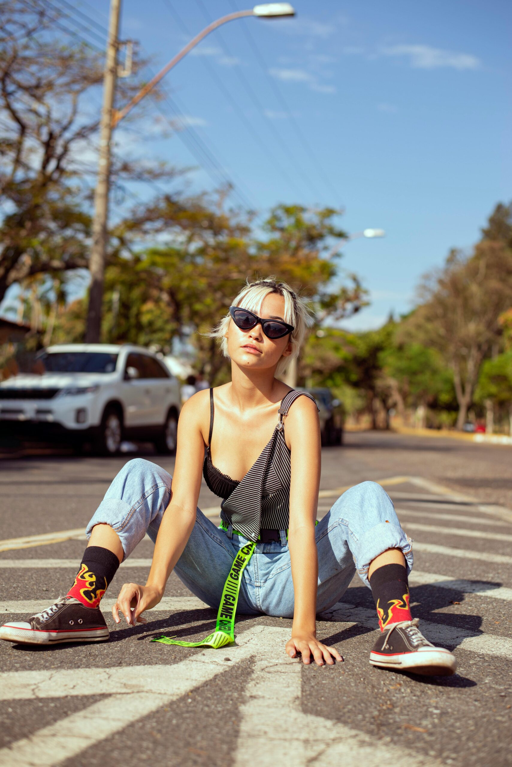 Model sitting on the ground wearing a black top, jeans, socks that have a fire pattern, black shoes and a pair of sunglasses.
