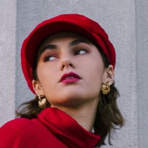 Close-up of a person wearing a structured red hat with gold earrings.