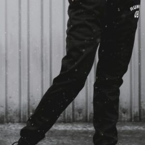 Black sweatpants with white text detail on the side, paired with sneakers.